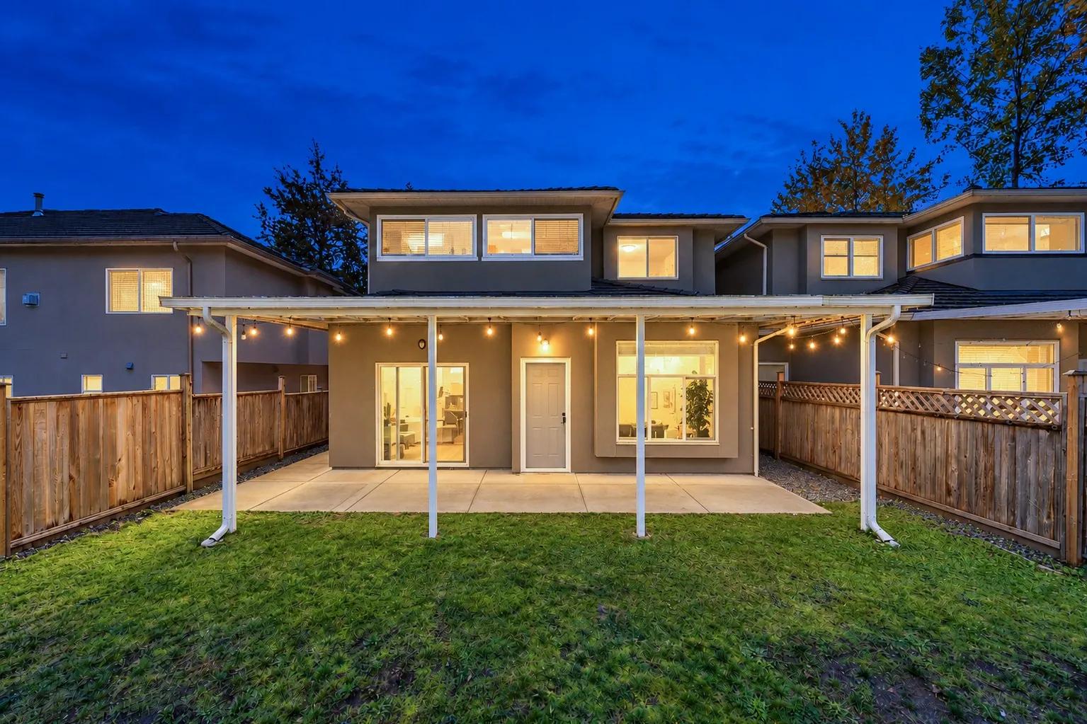 The back of the house at dusk: string lights under the patio cover, the windows lit