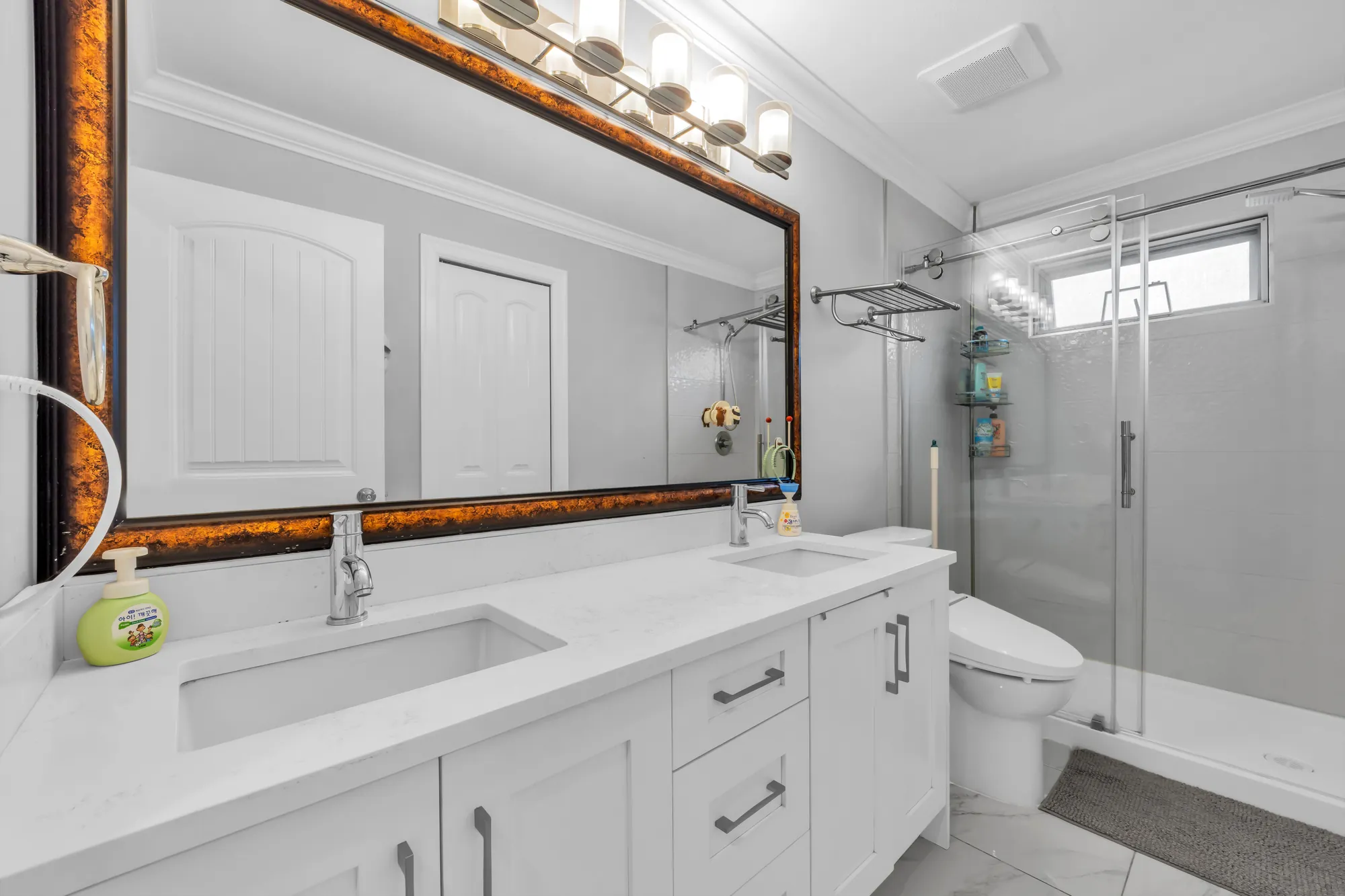 The upstairs bathroom: a double vanity with a white quartz top, a wide mirror, a glass shower, a toilet