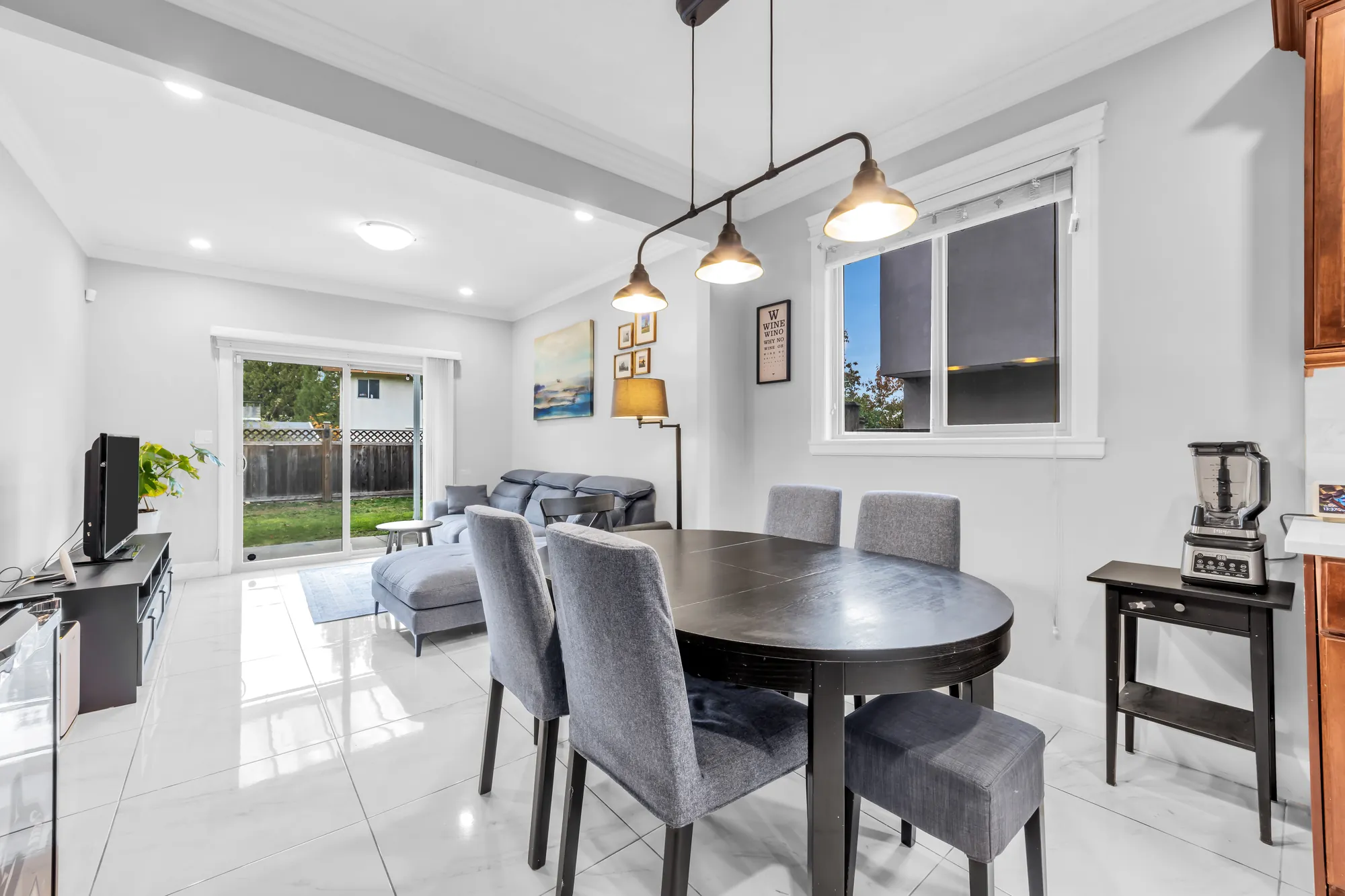 The breakfast area: a round table with grey chairs under three pendant lights, the family room beyond