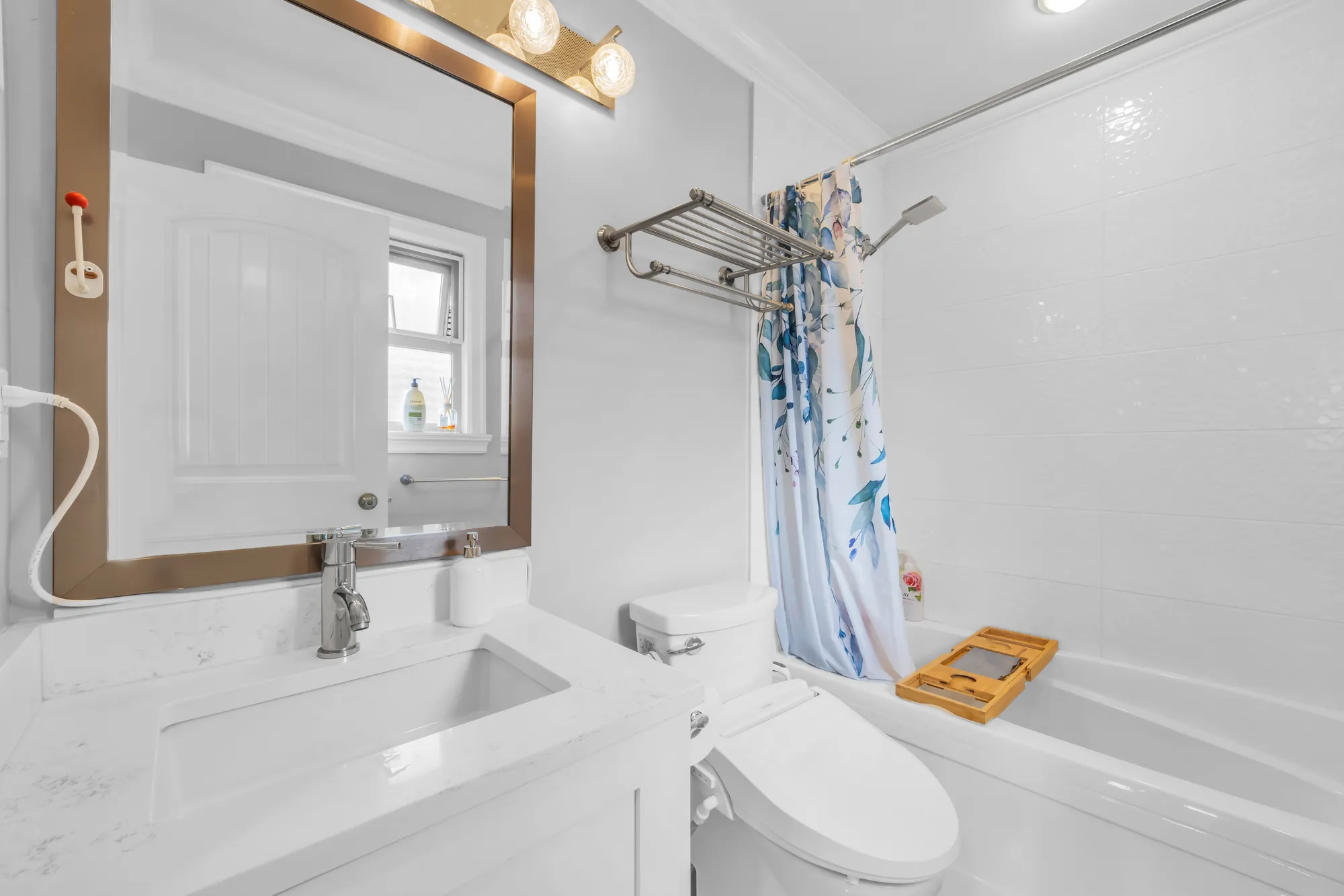 The primary bathroom: a white vanity, a toilet, a tub with a shower curtain, a large mirror