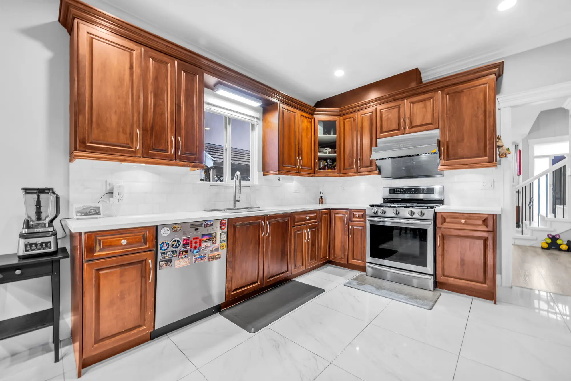 The kitchen: wood cabinets to the ceiling, white counters and a white tile backsplash, a stainless gas range and hood, a dishwasher