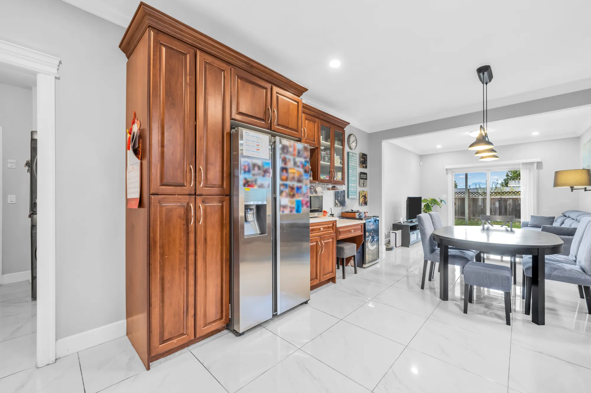 The kitchen toward the breakfast area: a stainless double-door fridge in tall wood cabinets, the breakfast table and the family room