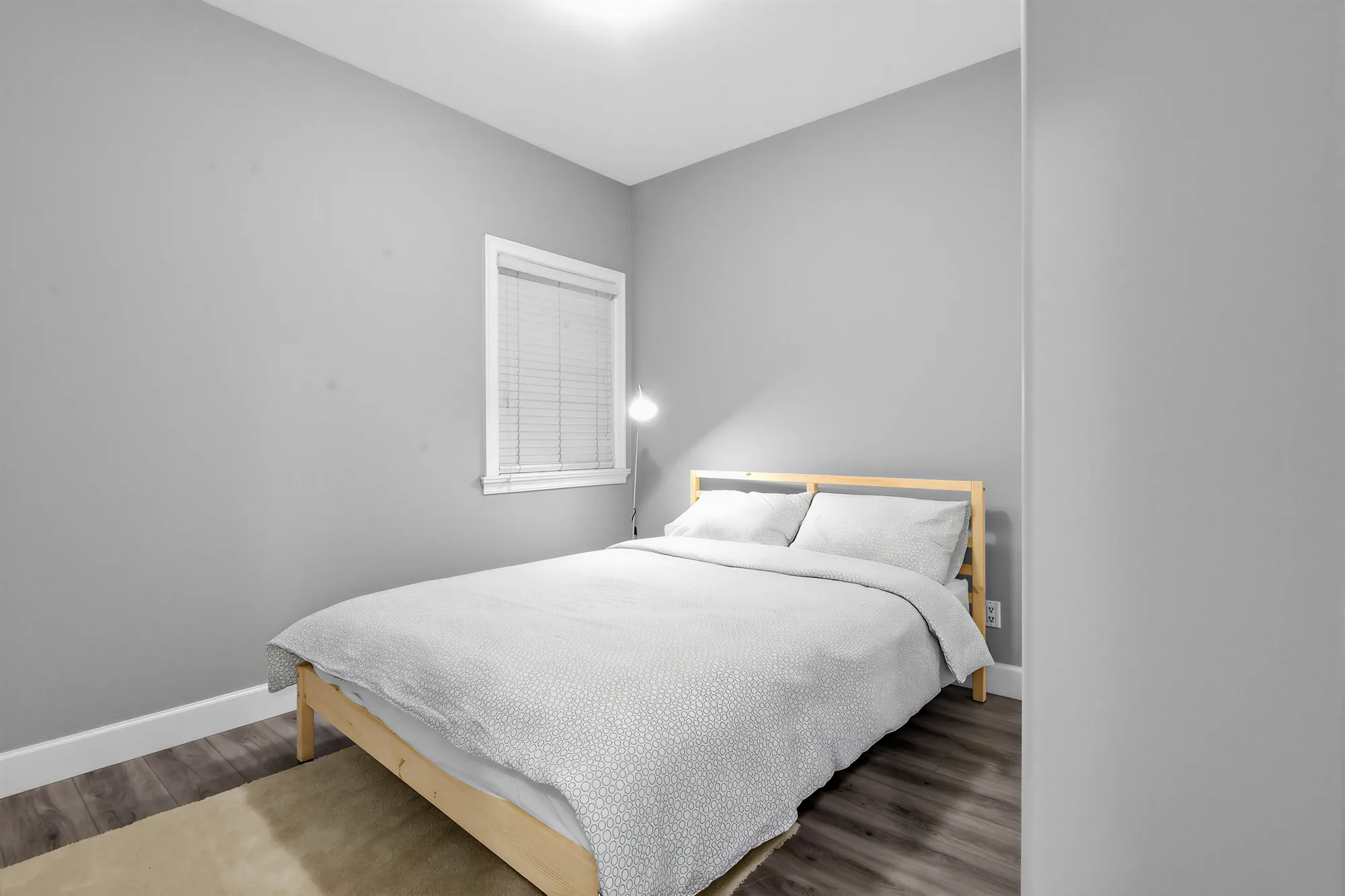 A bedroom in the guest suite: a pine bed with white bedding, a window with blinds, grey walls