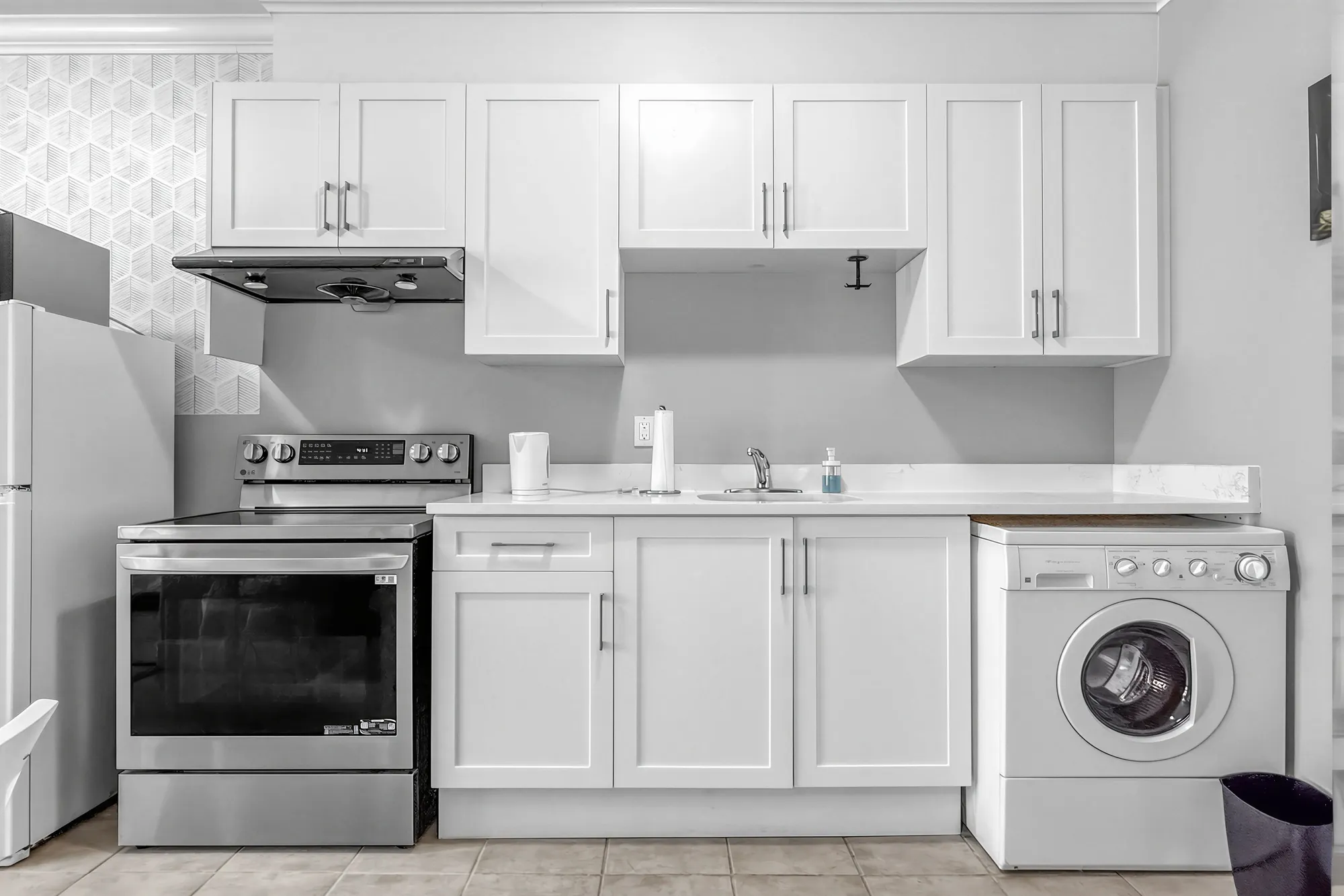The guest suite's kitchen: white shaker cabinets, a stainless range and hood, the sink, the washer