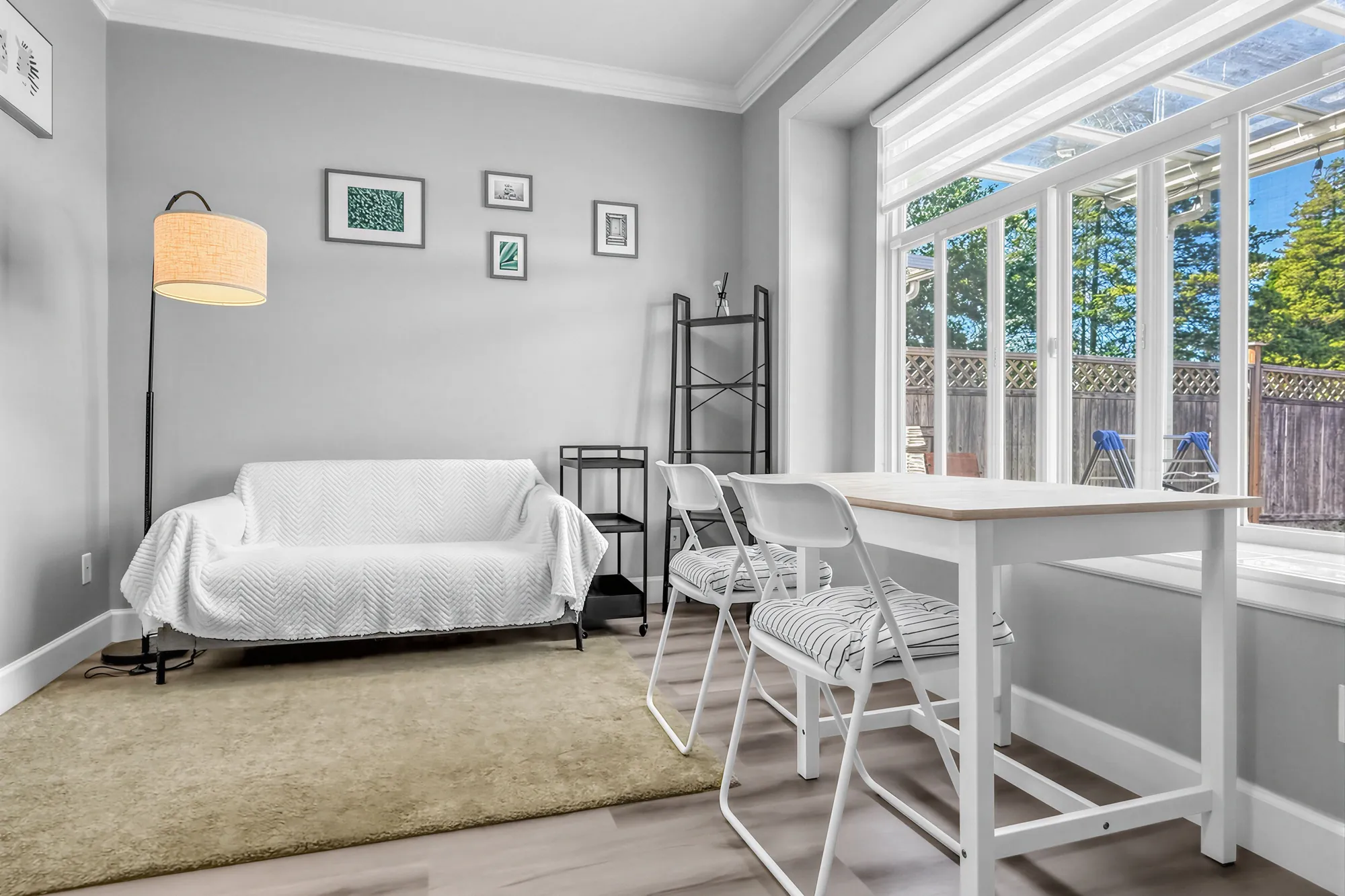 The guest suite's living area: a loveseat under a white throw, a small table and folding chairs, a wide window onto the yard